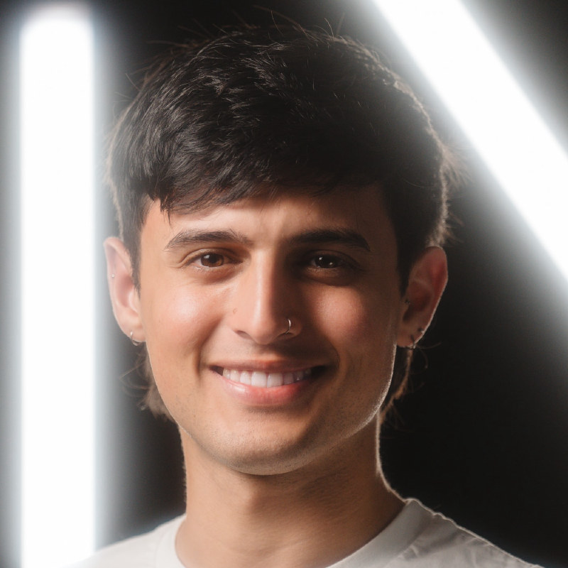 A studio portrait: a smiling man in a white T-shirt against a dark background.